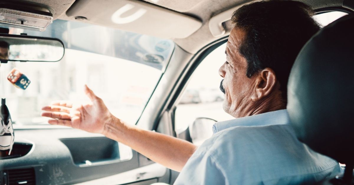 older man sitting in the passenger seat, gesturing where the driver should go